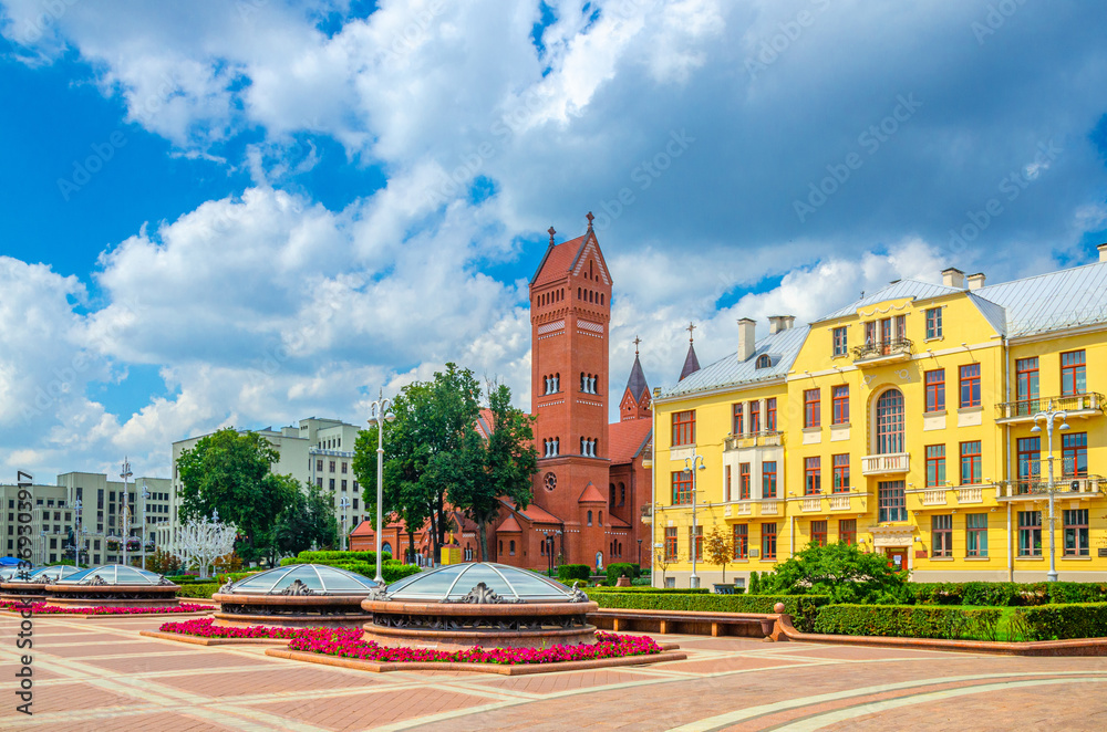 Saints Simon and Helena Roman Catholic church Red Church and Government House on Independence Square in Minsk city historical centre, blue sky white clouds in sunny summer day, Republic of Belarus