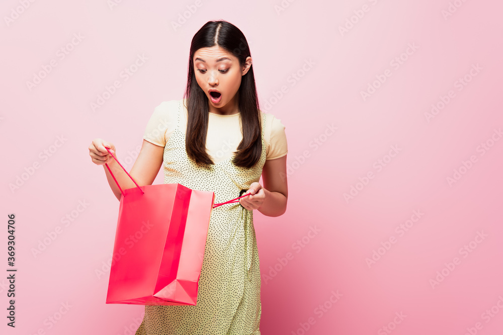 shocked young asian woman looking at shopping bag on pink shocked young asian woman looking at shopping bag on pink
