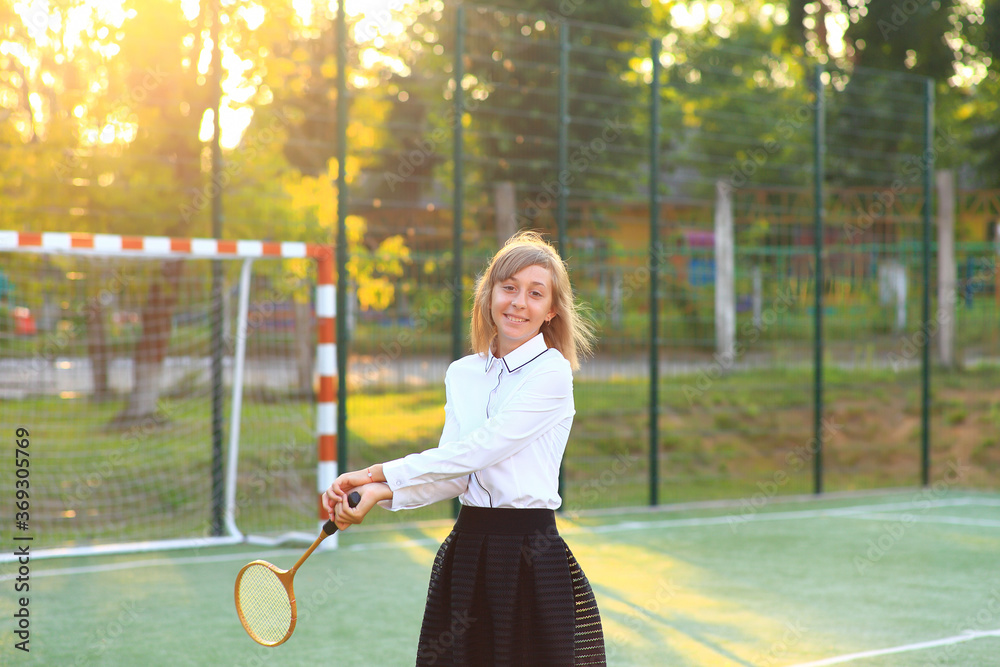 A girl in a school uniform with a racket in her hands on the football field.