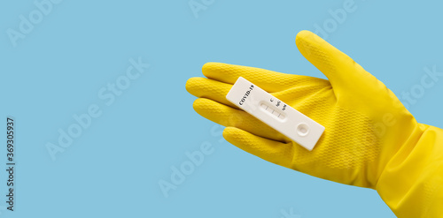 Unused covid-19 test in hand on a blue background. A hand in a yellow protective glove holds a test cassette for coronavirus.