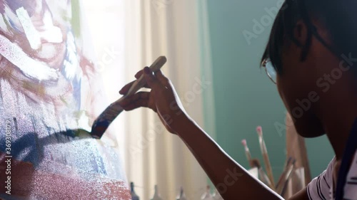 Young black woman artist is working on her new project, painting beautiful vibrant abstract picture on canvas, working with the bottom of the picture, applying paint, Close up, Slow motion.