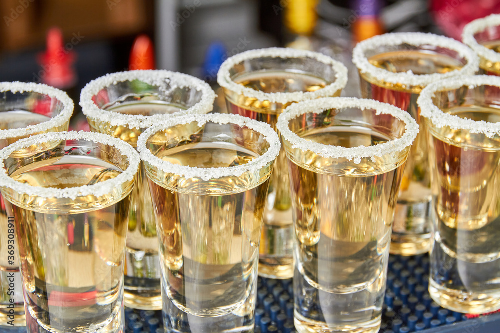 Golden tequila in salt frosted shot glasses on the bar. Close-up, selective focus