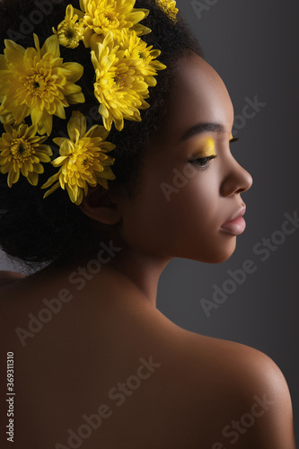 Young african american woman with artistic make-up and flowers in hair on grey background.