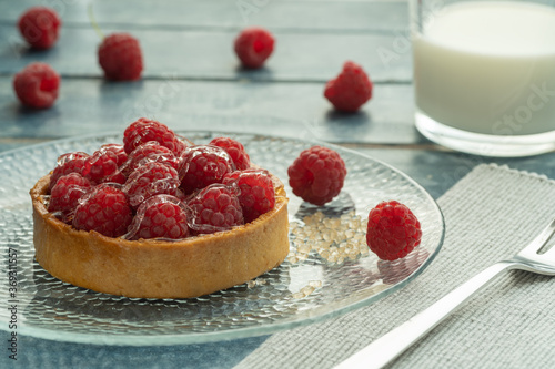 Raspberry tartlets served on a transparent plate with brown sugar. Glass of milk on a light blue wooden background.