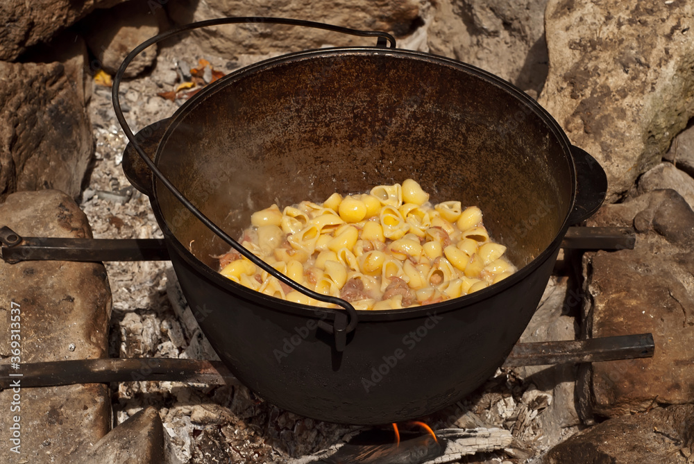 Pasta with meat is cooked in a cast iron cauldron. Cooking on a campfire. Pasta with meat is cooked in a cast iron cauldron. Cooking on a campfire.