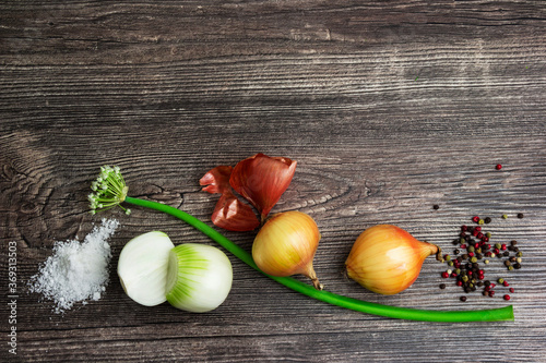 Pile of fresh spring golden and green onion with peel, white salt, black pepper on wooden background