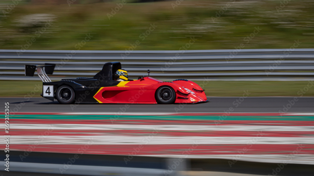 A panning shot of a red and black racing car as it circuits a track.