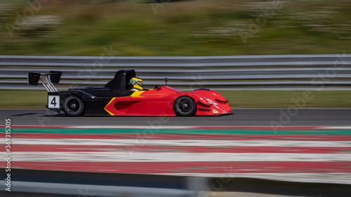A panning shot of a red and black racing car as it circuits a track.
