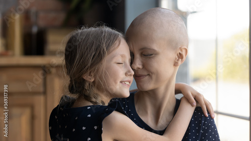 Happy young Caucasian cancer patient sick mother and little daughter hug show love and care, supportive small girl child embrace caress ill hairless mom suffer from oncology, feel grateful thankful