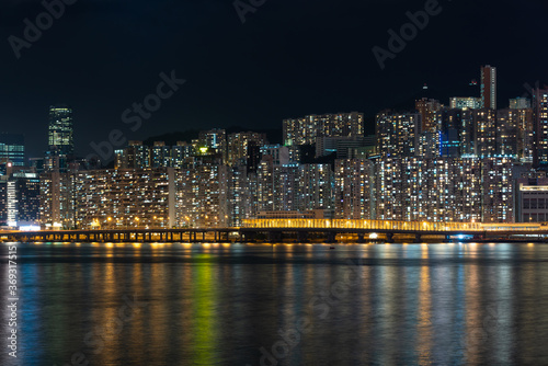 Hong Kong cityscape at night over Victoria Harbor with clear sky and urban skyscrapers.