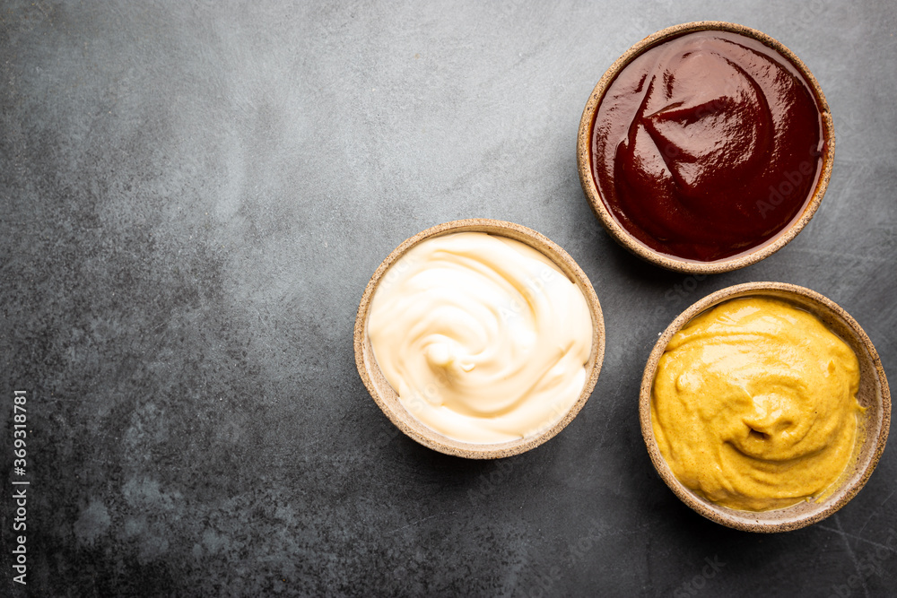 Classic set of sauces, American yellow mustard, ketchup, barbecue sauce, mayonnaise on black stone background, top view with copy space. Classic set of sauces, American yellow mustard, ketchup, barbecue sauce, mayonnaise on black stone background, top view with copy space.