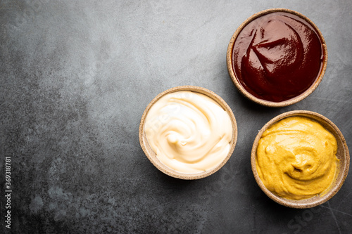 Classic set of sauces, American yellow mustard, ketchup, barbecue sauce, mayonnaise on black stone background, top view with copy space.