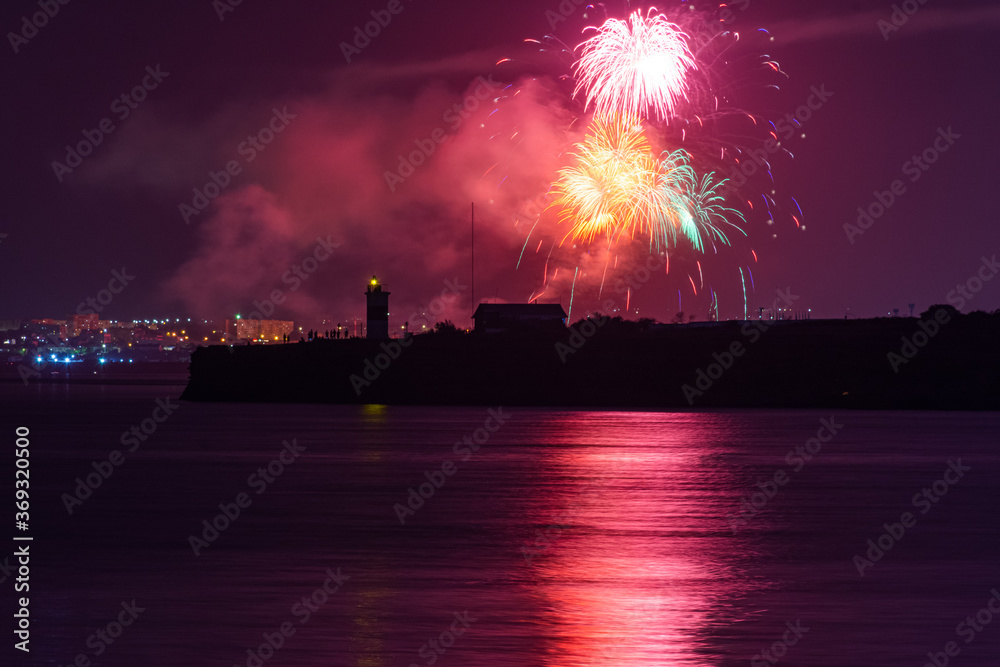 Festive salute over the city of Sevastopol on the day of the Navy. Bright multicolored flashes of fireworks. The concept of the celebration. Night shooting of the city. Silhouette of the lighthouse.