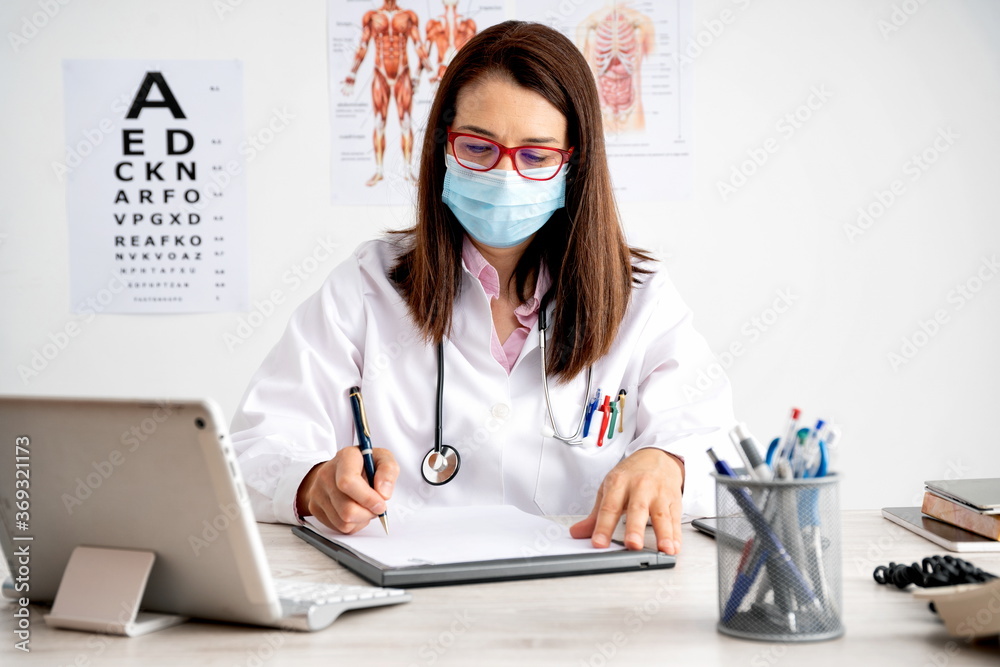Female doctor with mask working in her office filling out papers Female doctor with mask working in her office filling out papers