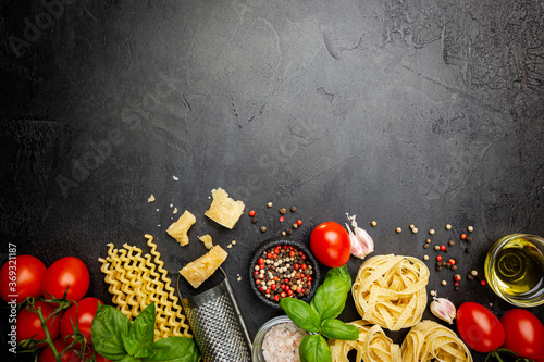 Pasta background. Several types of dry pasta with vegetables and herbs on black background. Free space for text. Top view