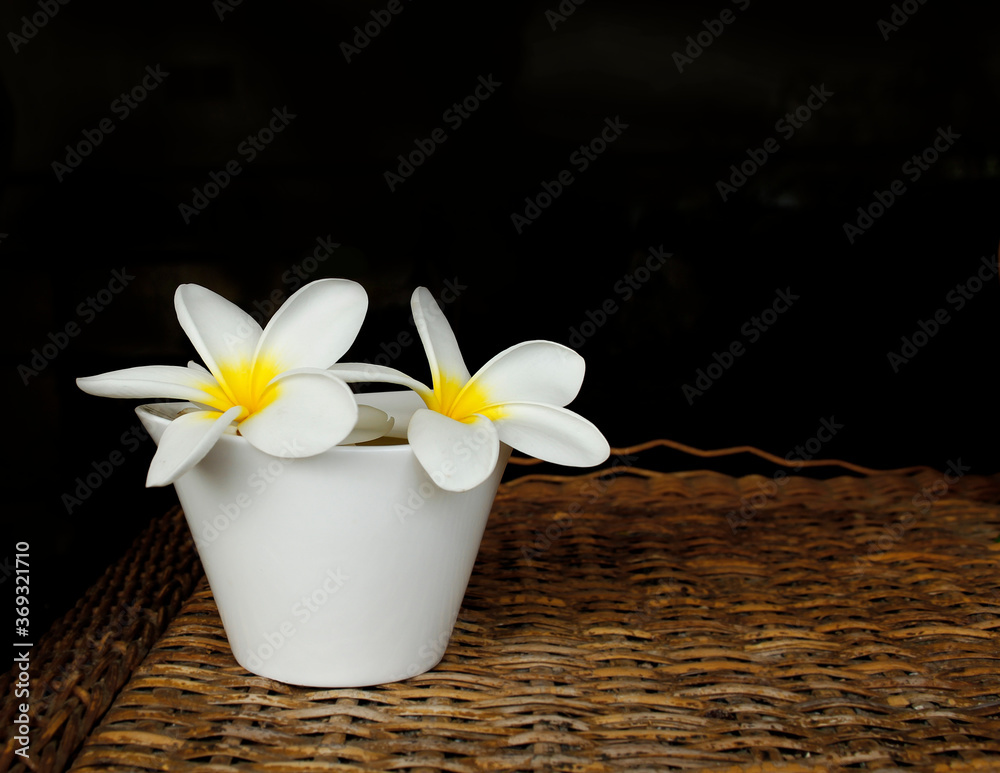 Recipiente de amapolas blancas sobre una mesa de rafia en un spa con fondo negro. Recipiente de amapolas blancas sobre una mesa de rafia en un spa con fondo negro.