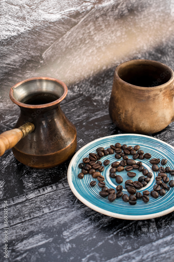 Clay cup with cezve and coffee beans on a blue saucer. Coffee concept. Vertical photo Clay cup with cezve and coffee beans on a blue saucer. Coffee concept. Vertical photo