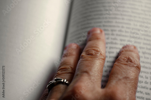 Primer plano de unos dedos de mujer mayor sobre un libro abierto. © YamilaG