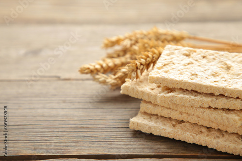 A slices of wheat crispbread with spikelets of wheat on grey wooden background.