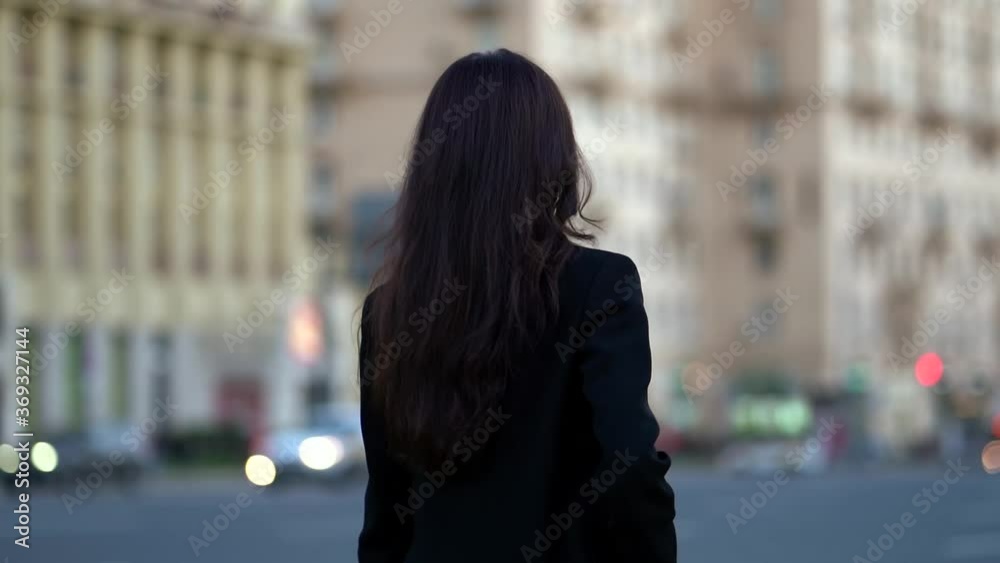 Close-up portrait of a bright dark-haired girl in a black jacket, she is against the background of a European city, walking, in the background passing transport Close-up portrait of a bright dark-haired girl in a black jacket, she is against the background of a European city, walking, in the background passing transport