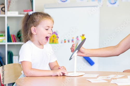 developmental and speech therapy classes with a child-girl. Speech therapy exercises and games with a mirror and cards photo