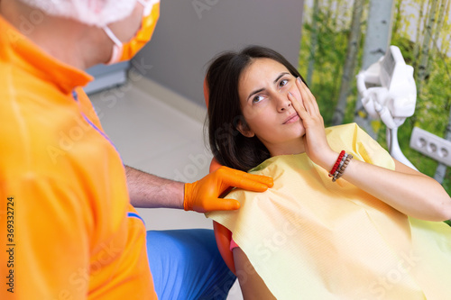 Young woman with toothache sitting in chair in dental office. Girl pressing her cheek due to bad tooth pain.