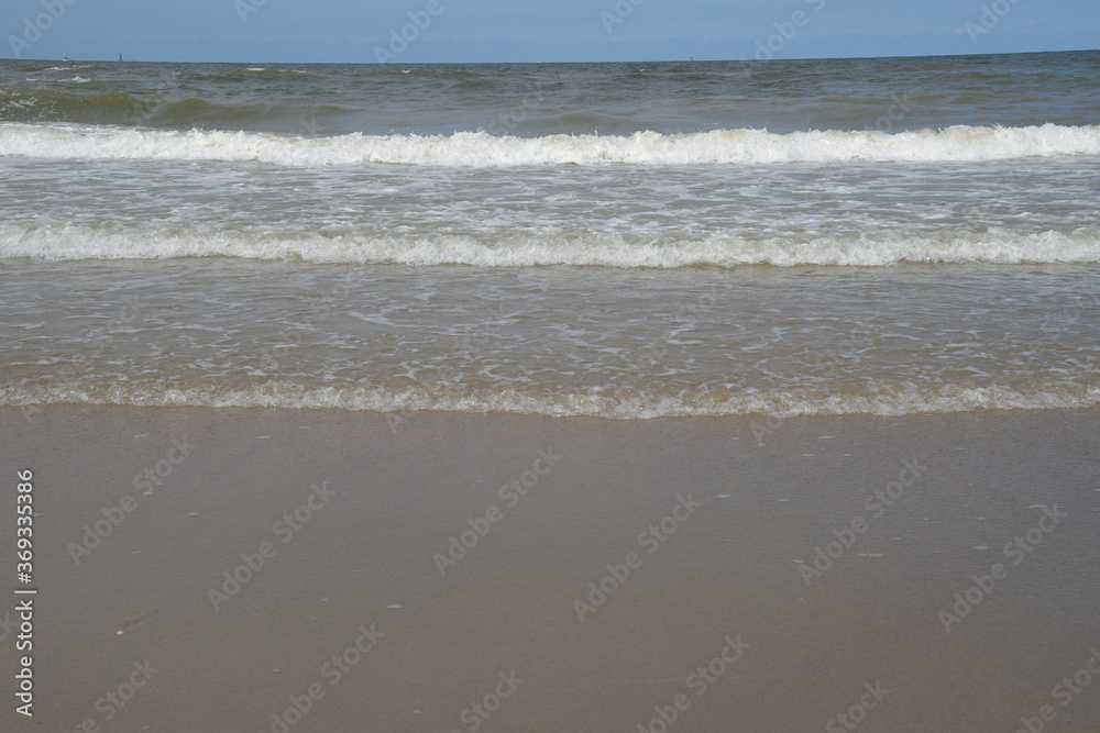 Das blaue Meer wird von mehreren weißen Wellen aufgewühlt. Am Horizont sieht man ganz klein mehrere Segelschiffe. 