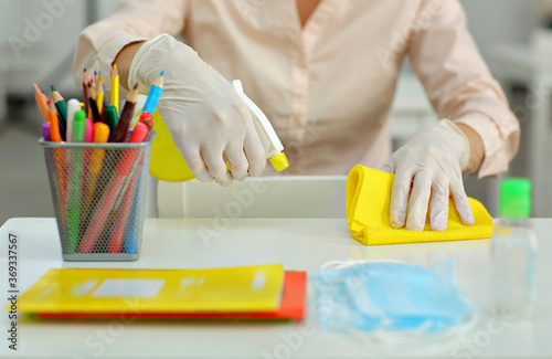 woman in a medical gloves treats and disinfects desk at school before classes
