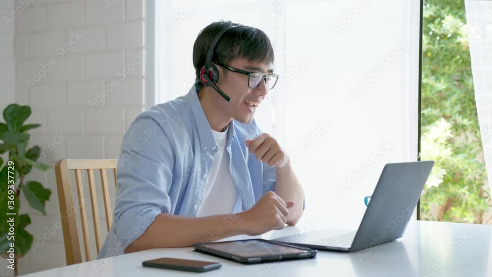 Medium shot : Asian man in casual shirt sitting telework or webinar on laptop computer. Businessman video conference using laptop and tablet online meeting.Working from home and Working remotely. Medium shot : Asian man in casual shirt sitting telework or webinar on laptop computer. Businessman video conference using laptop and tablet online meeting.Working from home and Working remotely.
