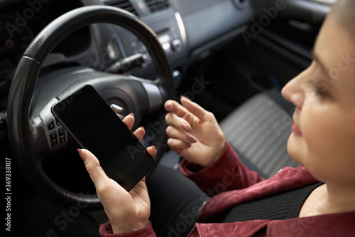 People, age, transportation, modern lifestyle and technolgy concept. High angle view of stylish gray haired mature woman sitting in driver's seat holding smart phone, setting online GPS navigation app