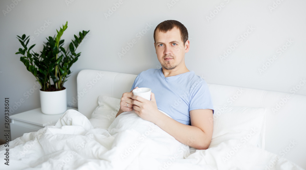 good morning concept - handsome man sitting in bed and drinking coffee good morning concept - handsome man sitting in bed and drinking coffee