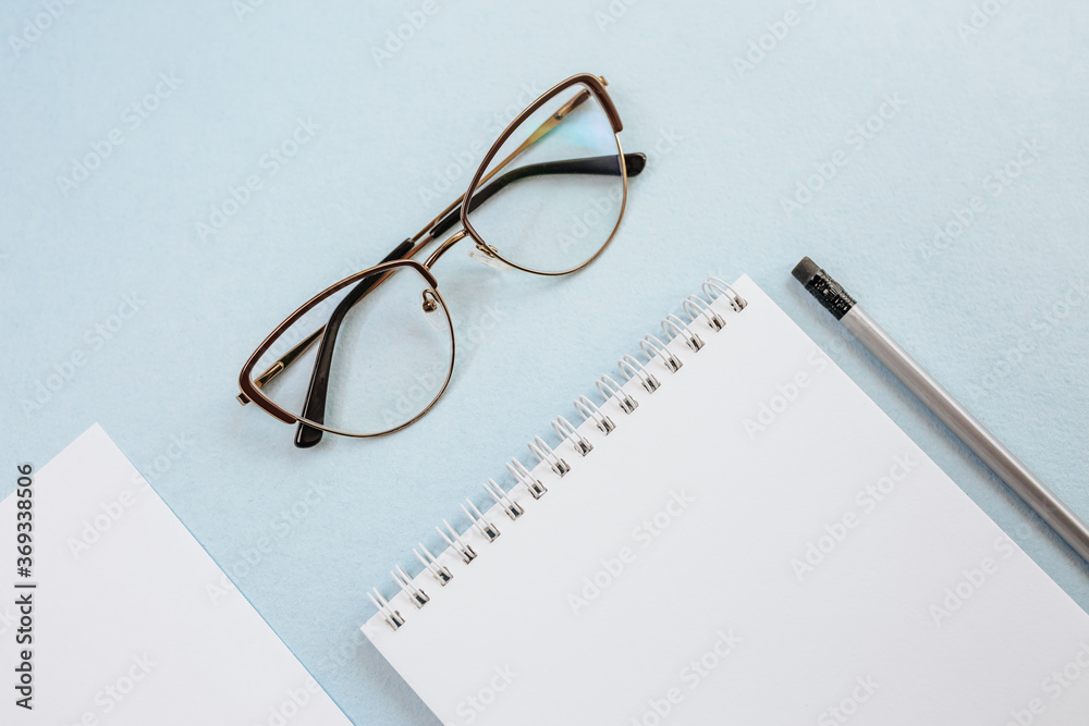 Office concept. Workspace with glasses, notebook and pencil. Copy space white and blue background. Office concept. Workspace with glasses, notebook and pencil. Copy space white and blue background.