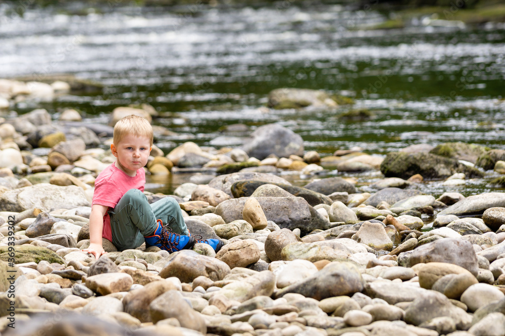 child sat on rocks at waters edge child sat on rocks at waters edge