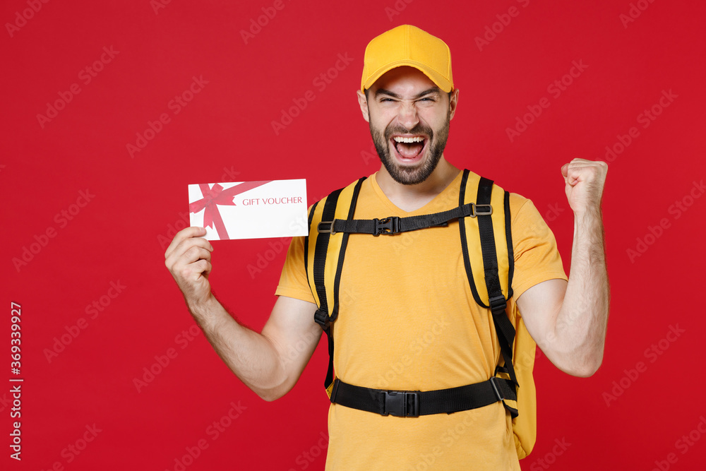 Delivery man in yellow cap t-shirt uniform thermal bag backpack with food hold certificate isolated on red background studio Guy male employee work courier Service coronavirus covid-19 virus concept