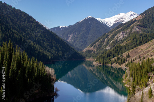 Mountain lake against the background of snow-capped peaks. There is a dense forest along the banks.