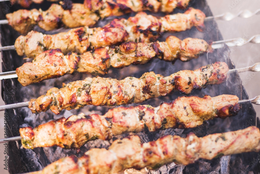 Preparation of shish kebab on barbeque over charcoal. Closeup of grilled meat cooking on metal skewer, smoke. Summer picnic/BBQ. Tasty street food. Traditional eastern dish. Natural bluerred backdrop.