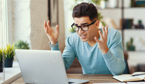 Angry ethnic freelancer using laptop at home