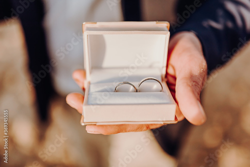 Close-up view of man's hand holding white box with elegant wedding rings. Outdoor marriage jewelery concept.