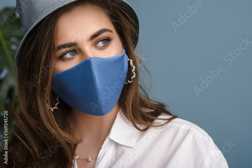 Woman wearing stylish protective blue face mask, trendy bucket hat, pearl earrings. Fashion accessory during quarantine of coronavirus pandemic. Close up studio portrait. Copy, empty space for text