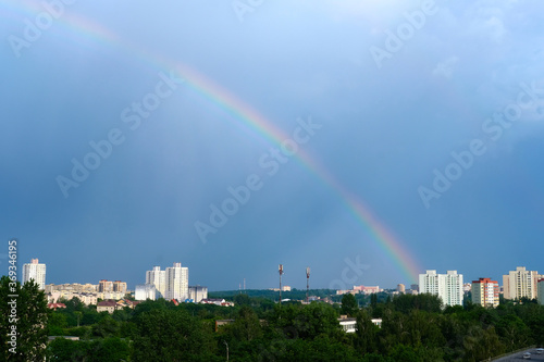 Bright multicolored rainbow on the houses of the city in the blue sky