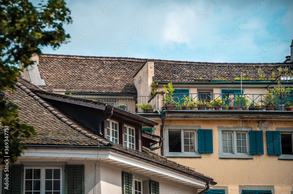 Zurich architecture. The facade of the house, windows with green shutters, brown tile roof. terrace decorated with flowers in pots.
