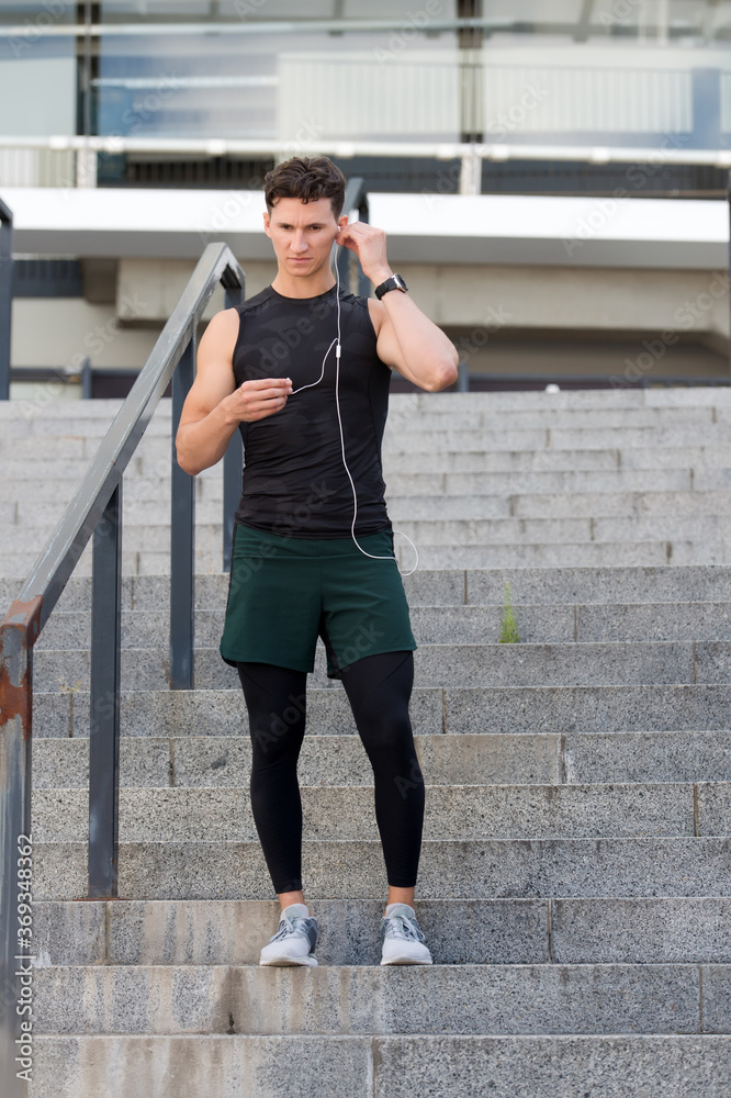 relax after challenging workout. Runner listens to music with headphones. Fitness sport man using headphones relaxing post-workout. Fit fitness sports model prepare music outside before jogging