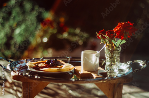 Still life shot of  breakfast tray silver platter with cup of coffee  roses and pancakes bathed in golden light lens flare