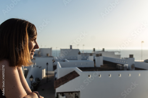 Fototapeta Naklejka Na Ścianę i Meble -  Attractive young female witnessing the sunset from a viewpoint located in a small village in Cadiz, Spain