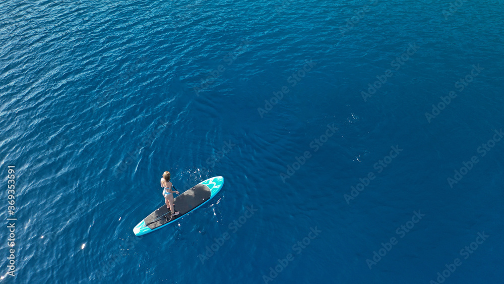 Aerial photo of fit woman paddling on a sup board in deep blue Aegean sea