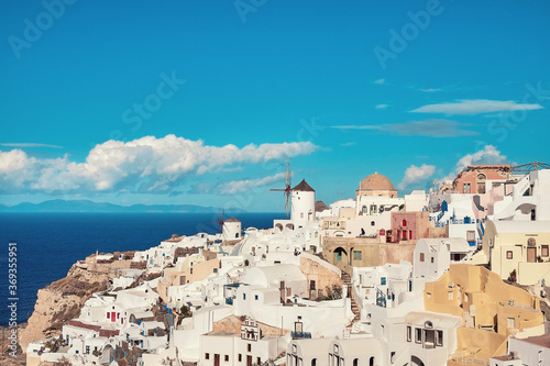 Clouds fly over white houses and old windmill in Oia village on Santorini, Greece