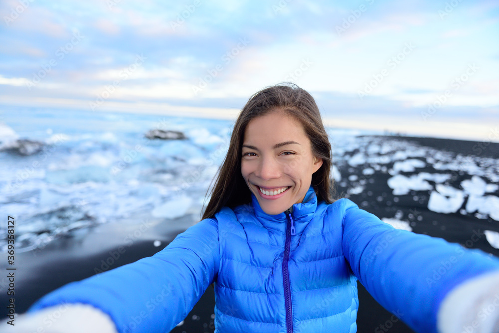 Adventure selfie by trave explorer woman on Iceland Diamond Beach. Woman tourist in amazing landscape Ice beach, Breidamerkursandur by jokulsarlon glacial lagoon / glacier lake nature.