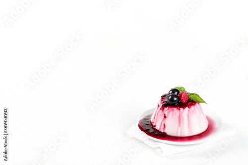 Panna cotta cream with berry sauce and fresh raspberries and black currants on a white background copy space