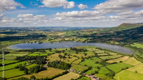 Aerial hyperlapse of clouds and a large lake in a rural, farming area (Llangorse Lake, Wales, UK)