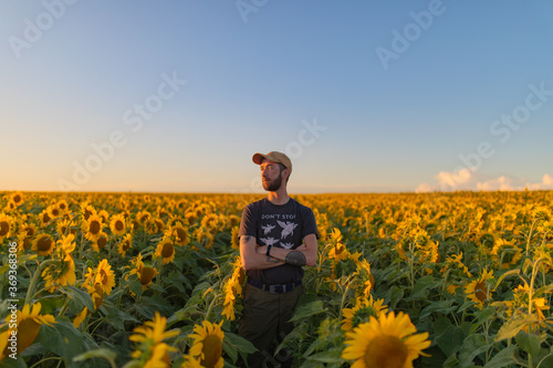 A young man in a dark T-shirt stands in the middle of a field with sunflowers and looks into the distance